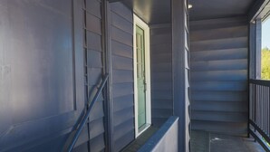 Un porche cubierto con una puerta verde, barandilla metálica y una escalera.