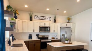 A modern kitchen with white cabinets, stainless steel appliances, a central island with stools, and a 'WELCOME' sign above.