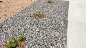 A modern house with a stone facade, a porch with a bench, and a driveway with gravel and small plants.