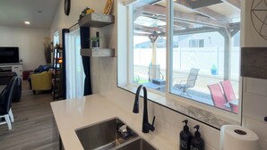 A modern kitchen with a large window, stainless steel sink, and built-in shelves.