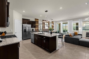 A modern kitchen with dark wood cabinets, a stainless steel refrigerator, and a granite countertop. - Last Minute Disney Getaway! Private Pool, Game Room & Themed Bedrooms. Book Now! #163035 (Orlando)