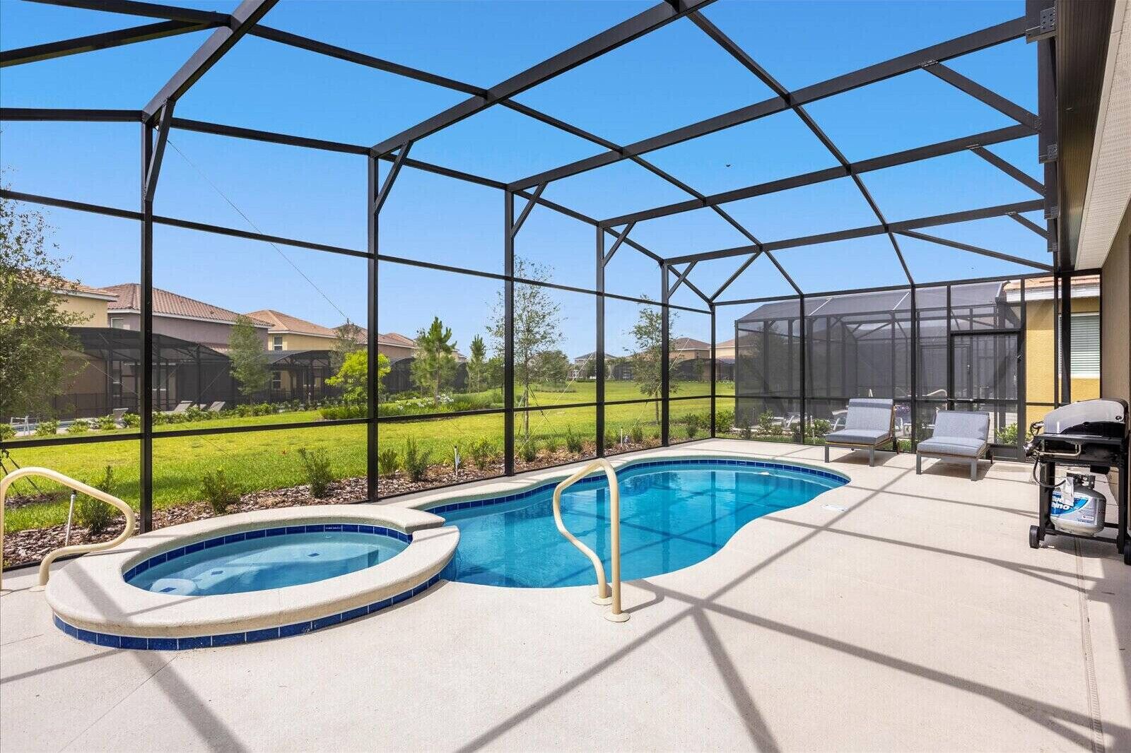 A covered outdoor swimming pool with lounge chairs and a grill area.