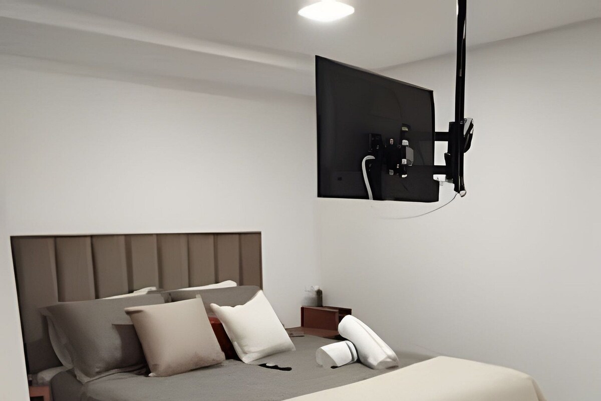 Ein modernes Schlafzimmer mit einem Bett, Nachttischen, einem an der Wand befestigten Fernseher und einem Sessel.