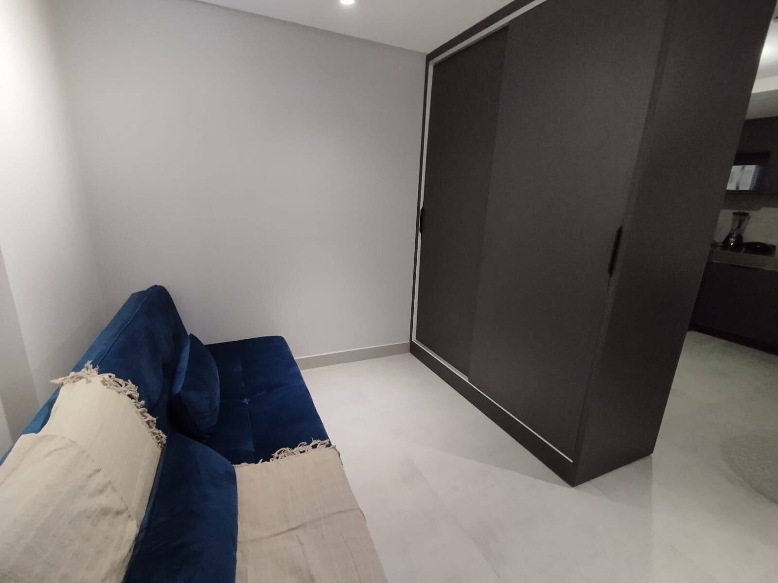Una habitación con un sofá azul, una puerta corredera oscura y una pequeña zona de kitchenette.