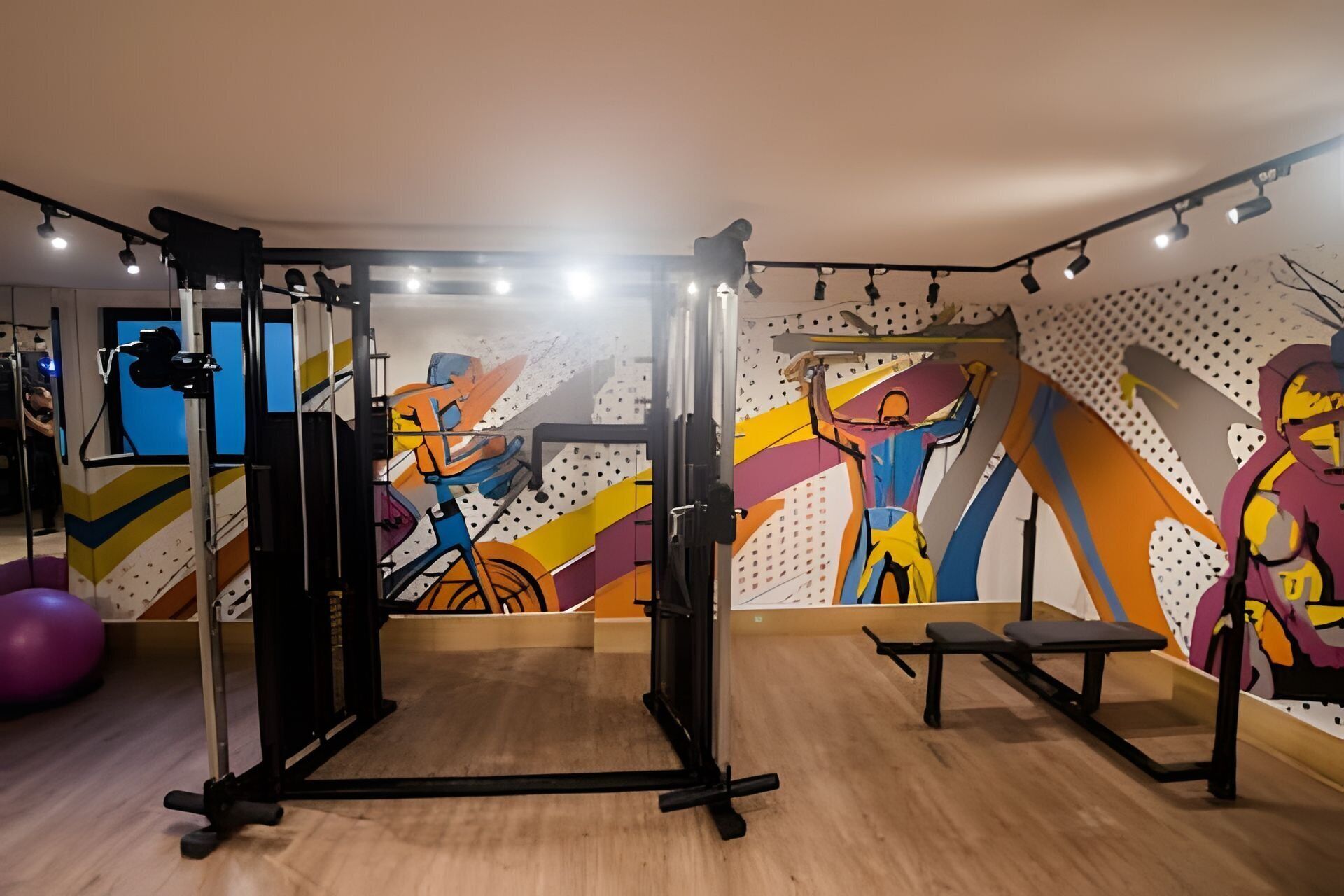 A gym with exercise equipment, a mirror, and a colorful abstract wall mural.