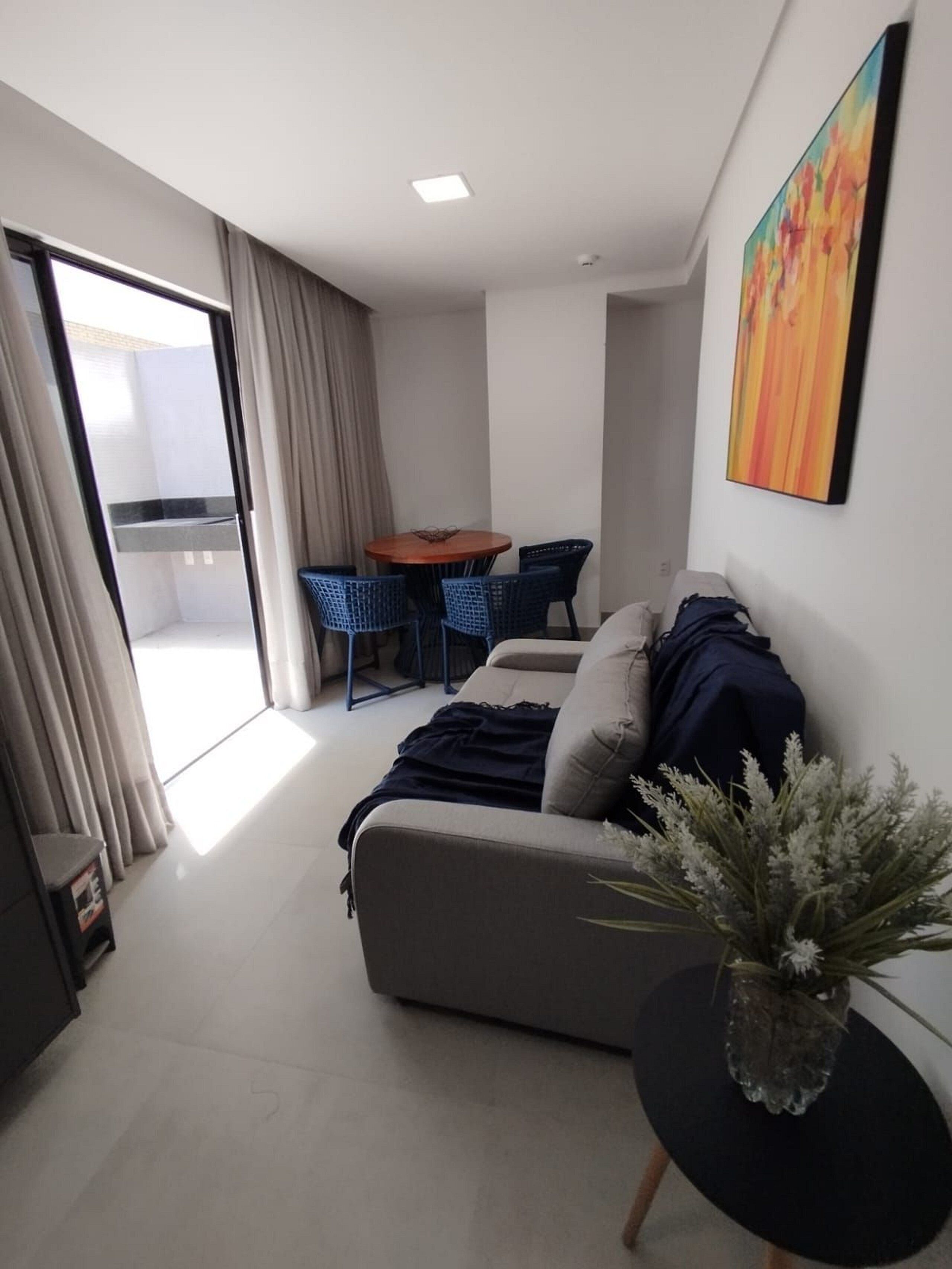 Een moderne woonkamer met een bank, een bijzettafeltje met een vaas en een eethoek met stoelen.