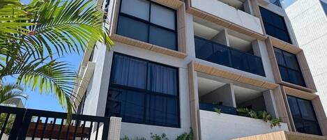 A multi-story building with balconies, a gated entrance, and a pool area.