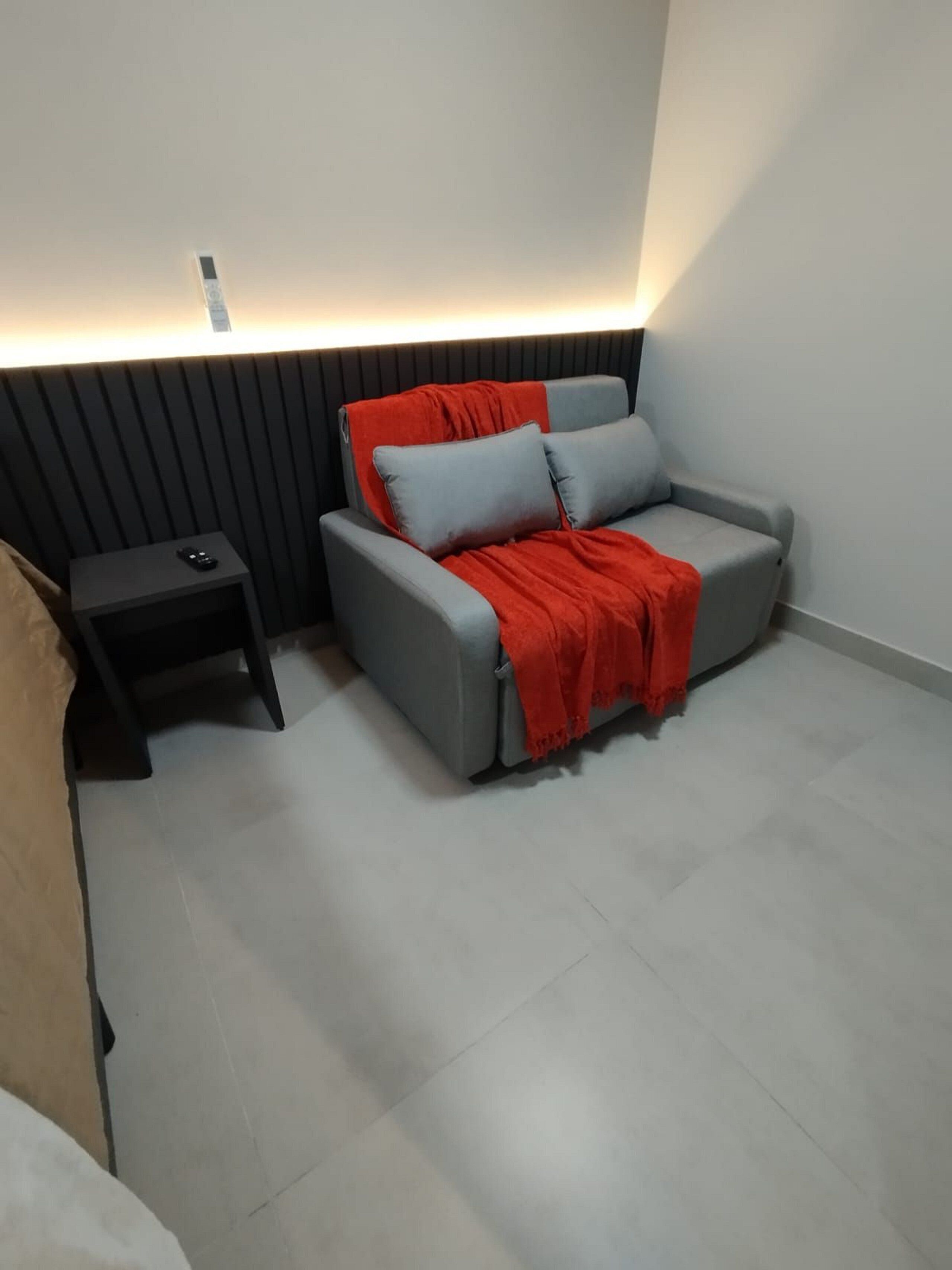 Une pièce moderne avec un canapé gris, un plaid rouge et une petite table d’appoint noire sur laquelle se trouve une télécommande.
