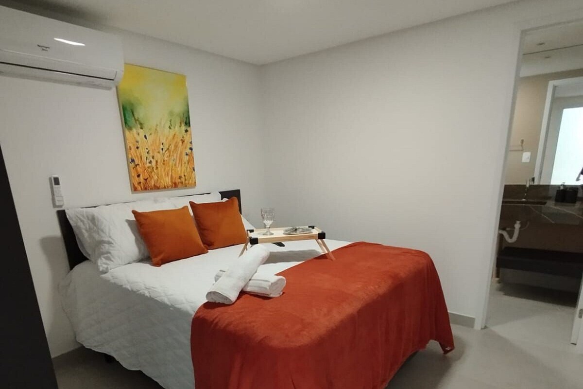 Ein modernes Hotelzimmer mit einem Bett, einem Nachttisch, einem Bild und einem durchgegangene Tür sichtbaren Badezimmer.