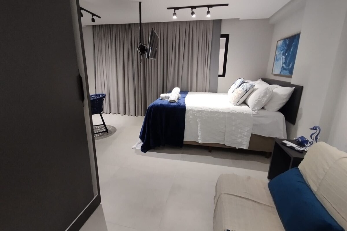 Ein modernes Hotelzimmer mit Bett, Stuhl, Schreibtisch und einem großen Fenster mit Vorhängen.