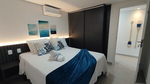 A modern hotel room with a large bed, a dark sliding door, a wall-mounted air conditioner, and a door with two paddles. - Ozean (João Pessoa)