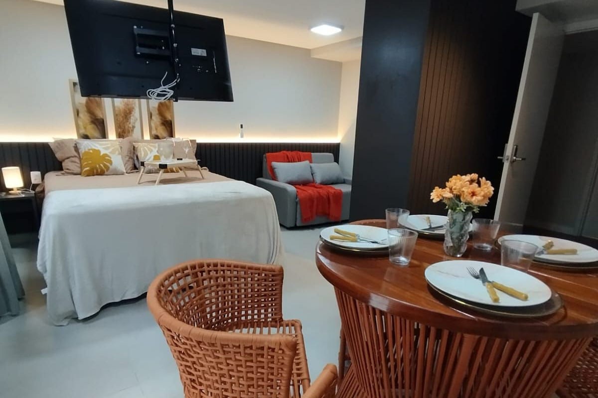 Ein modernes Hotelzimmer mit einem Bett, einem Esstisch mit Stühlen, einem an der Wand montierten Fernseher und Bildern an den Wänden.