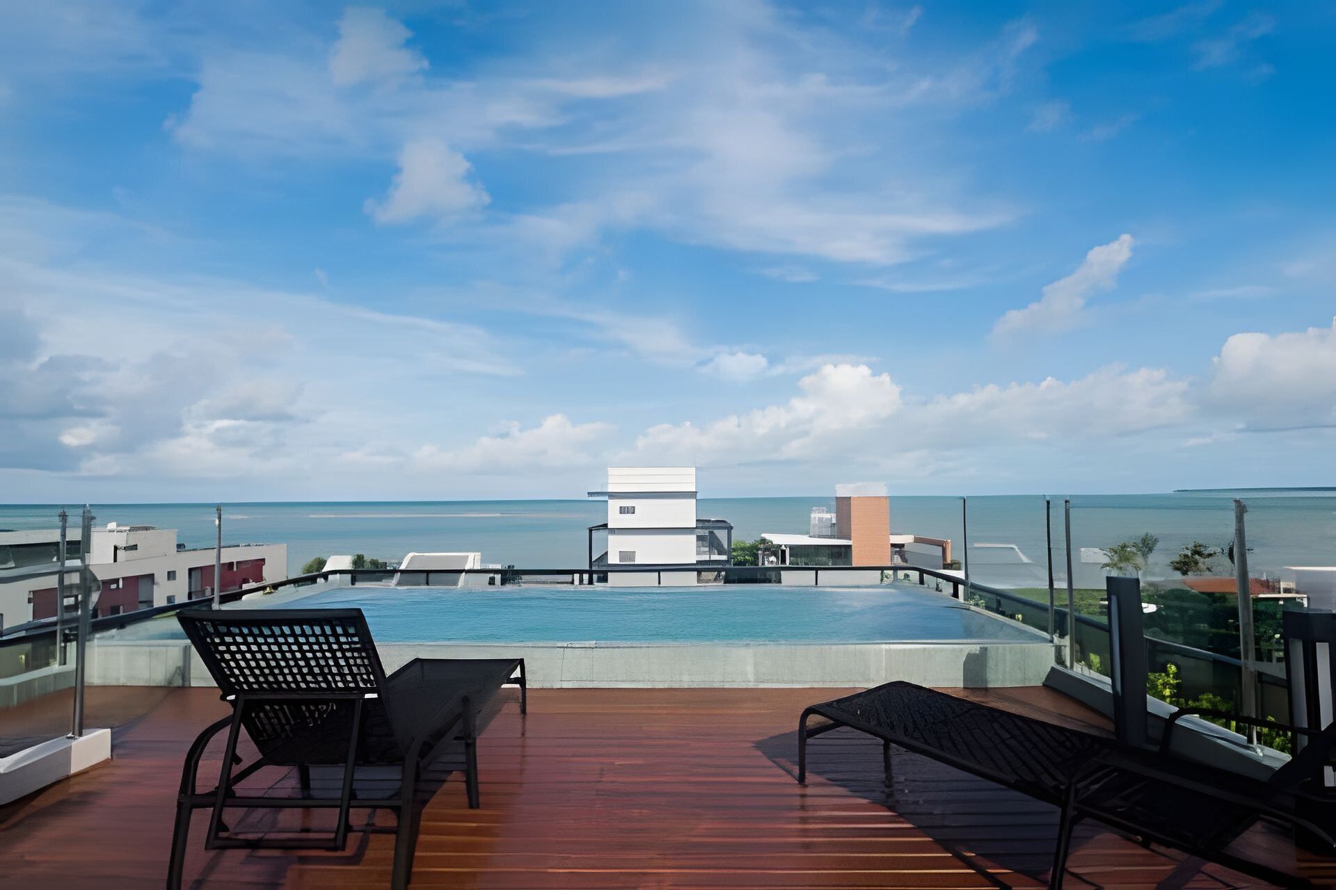 Una piscina en la azotea con dos sillones de descanso, vista al mar y cielo despejado.