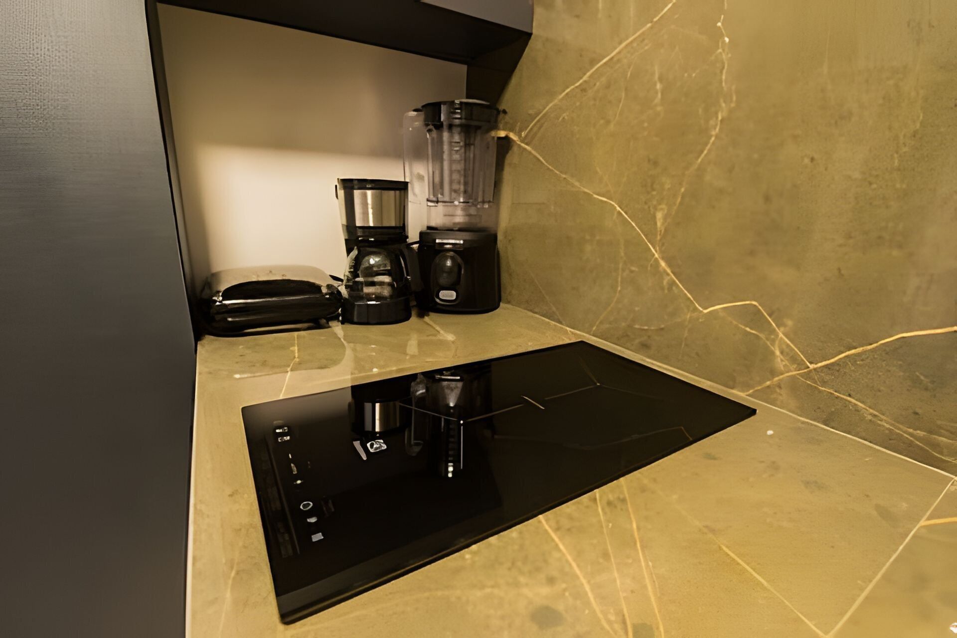 A kitchen with a black induction cooktop, a blender, and a coffee maker on a countertop.