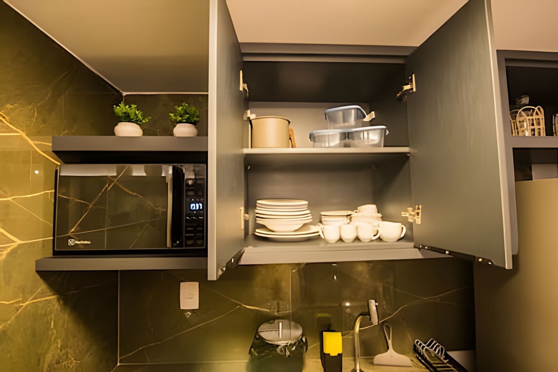 Una cocina con microondas, repisas con vajilla y una pequeña planta.