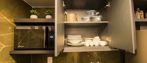 Una cocina con microondas, repisas con vajilla y una pequeña planta.