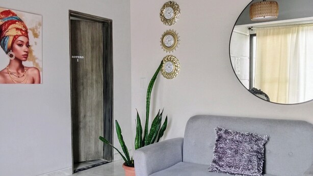 Ett modernt vardagsrum med en grå soffa, en stor spegel, en hängande lampa och en krukväxt.