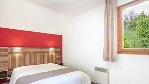 A hotel room with a bed, a red accent wall, a window with a view of greenery, and a radiator. - Duplex Chalet With Terrace (Gresse-en-Vercors)