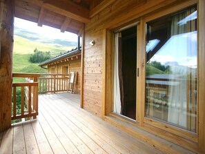 Een houten chalet met een houten terras, een schuifdeur en uitzicht op een groen landschap.