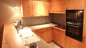A kitchen with wooden cabinets, a built-in oven, and a coffee maker. - Appartment in Vaujany (Les Deux Alpes)
