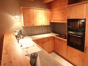 A kitchen with wooden cabinets, a built-in oven, and a coffee maker. - Appartment in Vaujany (Les Deux Alpes)