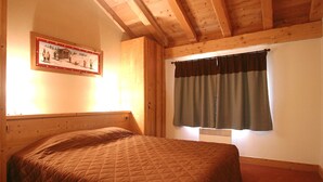 A single bed with a quilted blanket in a room with wooden beams, a window with curtains, and a framed picture on the wall. - Appartment in Vaujany (Les Deux Alpes)