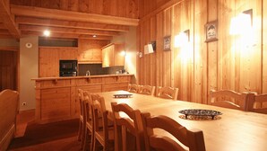 A wooden interior with a dining table and chairs, a kitchen area with wooden cabinets, and a wall-mounted light fixture. - Appartment in Vaujany (Les Deux Alpes)