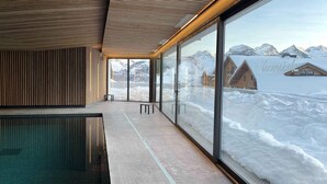 Una piscina interior moderna con amplios ventanales y vistas a montañas nevadas.