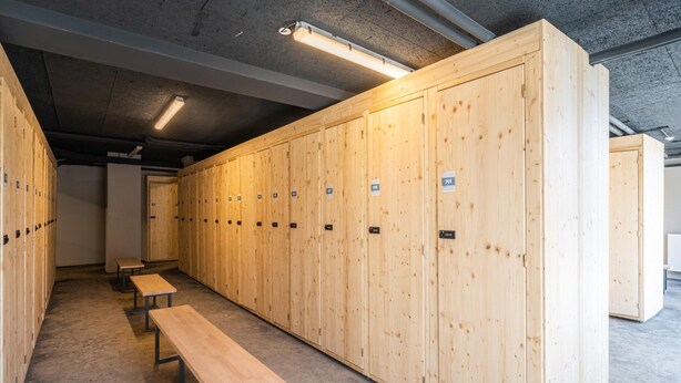 Un vestuario con taquillas de madera, bancos e iluminación fluorescente.