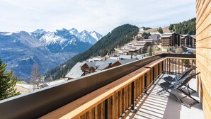 Un balcón de madera con vistas a un paisaje montañoso con picos nevados y una zona turística.