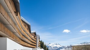 Un edificio moderno con fachada de madera y una vista despejada de montañas nevadas al fondo.