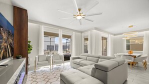 A modern living room with a sectional sofa, a flat-screen TV, and a ceiling fan. - Last Minute Disney Getaway! Private Pool, Game Room & Themed Bedrooms. Book Now! #173135 (Orlando)