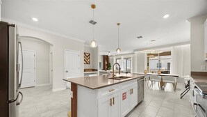 A modern kitchen with a central island, pendant lighting, and a dining area with a table and chairs. - Last Minute Disney Getaway! Private Pool, Game Room & Themed Bedrooms. Book Now! #173135 (Orlando)