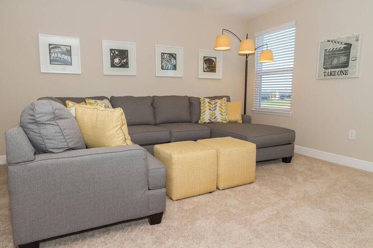 A living room with a sectional sofa, two ottomans, a floor lamp, and wall art.