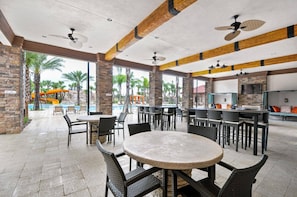 Ein Außenbereich mit einer Terrasse, runden Tischen und Stühlen, einem Pool mit Rutschen und einer Bar mit Sitzgelegenheiten.