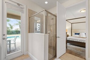 Una camera da letto con un letto a baldacchino, una cabina doccia in vetro e vista su una piscina.