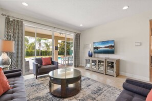 A living room with a sofa, a coffee table, a TV, and a sliding glass door leading to an outdoor area. - Last Minute Disney Getaway! Private Pool, Game Room & Themed Bedrooms. Book Now! #173143 (Orlando)