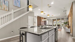 A modern kitchen with a central island, white cabinetry, and pendant lighting. - Last Minute Disney Getaway! Private Pool, Game Room & Themed Bedrooms. Book Now! #173149 (Orlando)