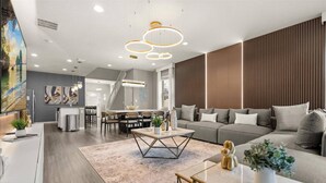 A modern living room with a sofa, coffee table, and dining area. - Last Minute Disney Getaway! Private Pool, Game Room & Themed Bedrooms. Book Now! #173149 (Orlando)