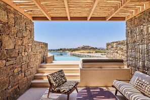 A stone-walled outdoor seating area with a pool, a wooden pergola, and a view of the sea. - Fouquet's Mykonos (Mykonos)