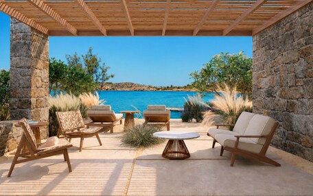 A covered outdoor seating area with stone walls, a view of the sea, and a clear sky.