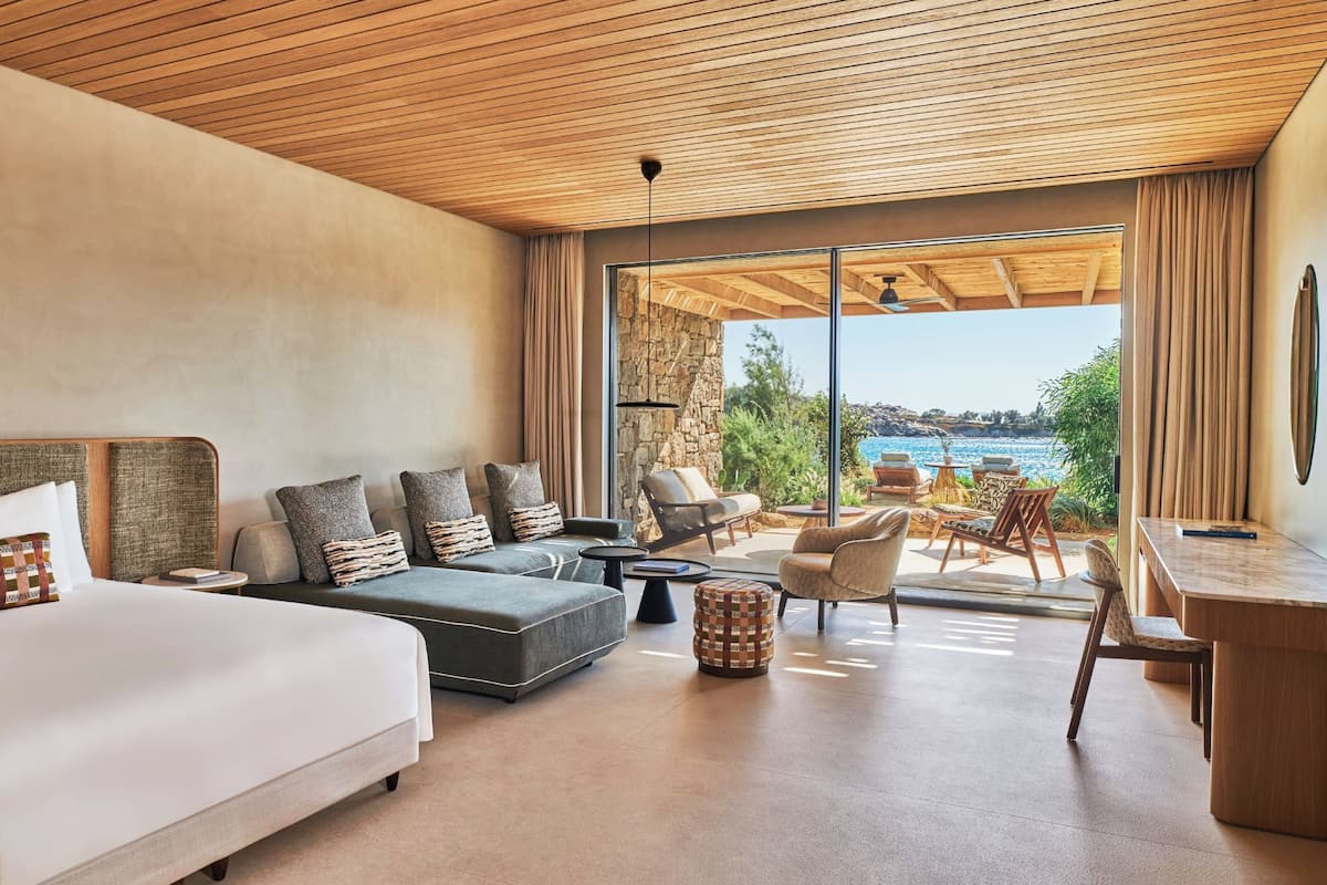 Una habitación de hotel moderna con una cama grande, un sofá, un comedor y vistas al mar.