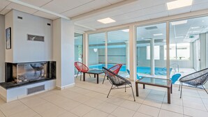 A modern indoor pool area with glass walls, a fireplace, and several seating areas. - Ocean-view Duplex for 8 (Plougonvelin)