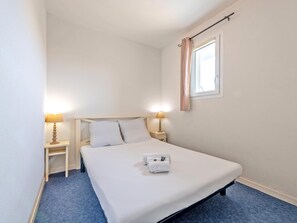 A single bed with a white mattress and pillows, two bedside tables with lamps, a window with curtains, and a blue carpet. - Ocean-view Duplex for 8 (Plougonvelin)