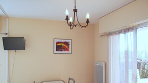 A room with a table and chairs, a television mounted on the wall, a framed picture, and a window with curtains. - Apartment “Soleil D'Oc 5” with Private Terrace and Wi-Fi (Cazaubon)