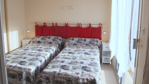 A room with two beds, a window with curtains, a bedside table with a lamp, and a wall-mounted light fixture. - Apartment “Soleil D'Oc 5” with Private Terrace and Wi-Fi (Cazaubon)
