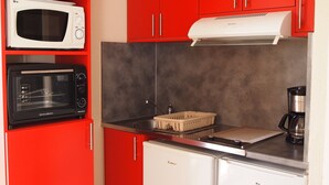 A compact kitchen with red cabinets, a white microwave, a coffee maker, and a small refrigerator. - Apartment “Soleil D'Oc 5” with Private Terrace and Wi-Fi (Cazaubon)