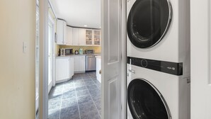 Een wasserij met twee gestapelde wasmachines, een keuken met witte kasten en een betegelde vloer.