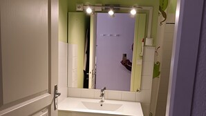 A bathroom with a white vanity, a mirror with lights, a green wall, and a shower with a frog design. - Apartment “Sauges 16” with Wi-Fi (Cazaubon)