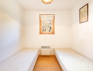 A small, single-room accommodation with two beds, a window with a view of a landscape, a radiator, and a framed picture on the wall. - Comfortable Apartment With Pool Access (Saint-Sorlin-d'Arves)